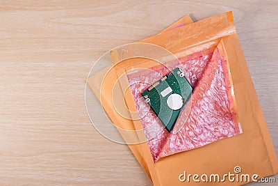 Yellow blank envelope with transparent bubble wrap or packaging shockproof on wooden table with storage hard disk. Stock Photo