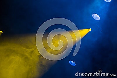 Yellow and blue light rays from the spotlight through theatrical smoke. Lighting equipment on the stage Stock Photo