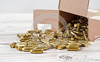 Yellow brass gun ammo spilled from paper carton box on white boar desk - close up Stock Photo