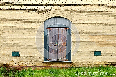 yellow brick building green boarded up door grass rusted Stock Photo