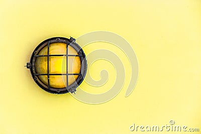 Yellow bulkhead light ship deck lamp surrounded by a metal rusted frame fixed to a painted light yellow pastel wall Stock Photo