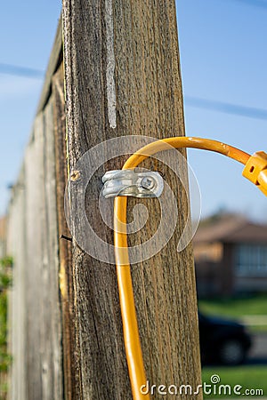 Yellow cable through metal bracket screwed to the support pole of a wooden fence Stock Photo