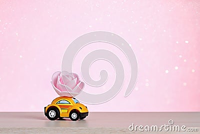 A yellow car carries a rose flower. Happy Valentine's Day, February 14th. Flower delivery. Valentine Day card. March 8 Stock Photo