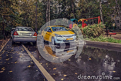 Yellow car rides in the yard on a wet road in the rain . Beautiful splashes of water from under the wheels. Stock Photo