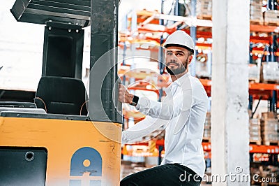 With yellow cargo moving machine. Storage worker is in the warehouse with bunch of products Stock Photo