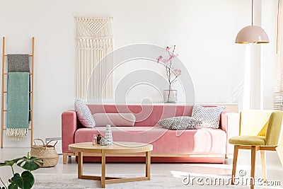 Yellow chair next to pink sofa and wooden table in pastel living Stock Photo