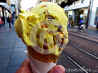 Vanilla orange ice cream cone held in male hand with blurry street background Stock Photo