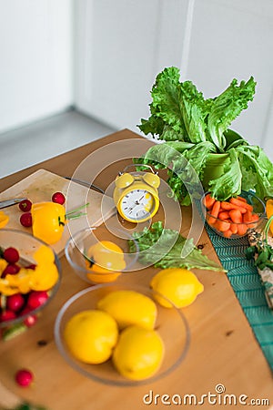 Yellow cooking timer between fresh cooking ingredients - vegetables, lemons and green salad Stock Photo