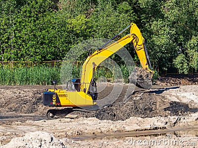 Yellow crawler excavator while working on a construction site. The machine lifted a bucket full of soil above the Editorial Stock Photo