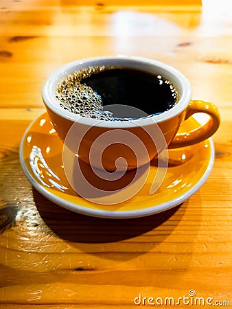 Yellow cup of black overflow coffee in small cafe Stock Photo