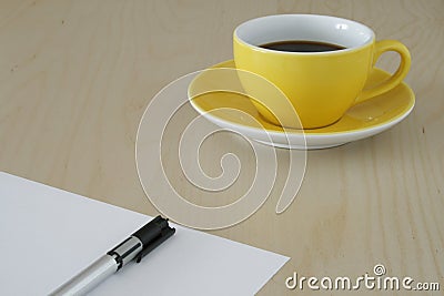 Yellow cup of coffee and a pen on paper Stock Photo