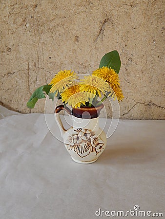Beautiful yellow dandelions in a vase on the table, spring flowers, clear weather. Stock Photo
