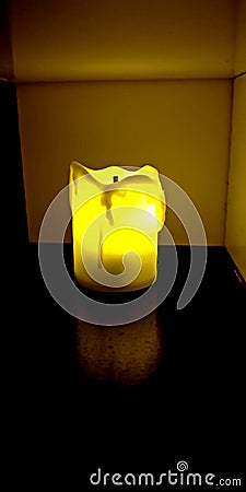 Yellow electric flameless battery powered candle shining in dark cabinet Stock Photo
