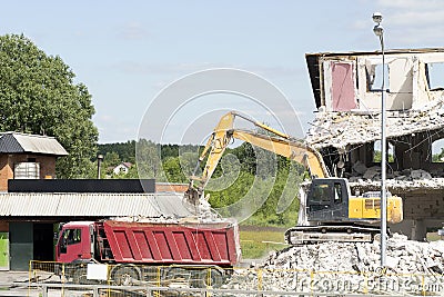 Yellow excavator loads construction debris into the truck. Technique destroys the building, is fittings, concrete and stones. Stock Photo