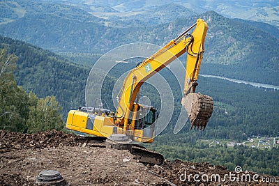 A yellow excavator works in the mountains. Construction of roads Stock Photo