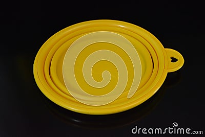 Yellow folding and multifunctional rubber plate, a bowl with a plastic edging on a black glossy surface. Stock Photo