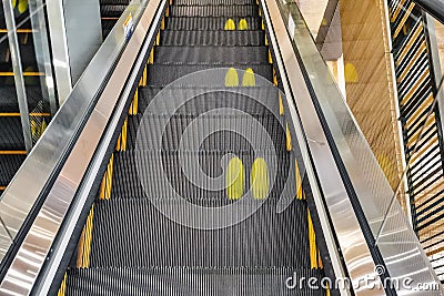 Yellow footprint symbol for social distancing on steps of escalator during Corona virus, social distancing and new normal concept Stock Photo