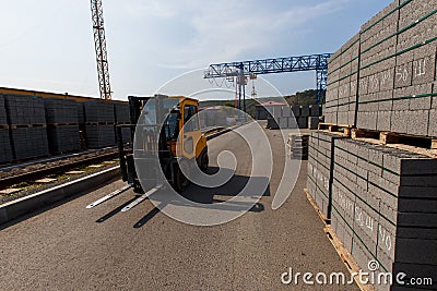 A yellow forklift rides through a warehouse past pyramid-packed packages of natural stone Editorial Stock Photo