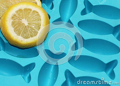 Lemon slices on turquoise wet shiny ice cube container with fish shapes for fish shaped ice cubes Stock Photo