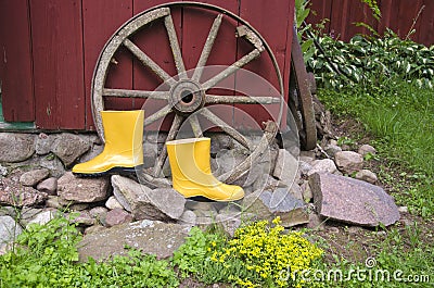 Yellow gardener rubber boots in farm near old wheel Stock Photo