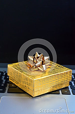 Yellow gift box sitting on a laptop computer keyboard close up Stock Photo