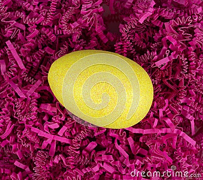 Yellow glitter easter egg atop dark pink shredded crinkle paper overhead view Stock Photo