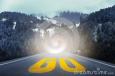 Yellow GO word written on highway road in the middle of empty asphalt road through the pine forest Stock Photo