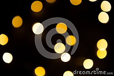 Yellow and gold lights garland in a blur on a black background. Bokeh of flying circles in the defocus. Festive atmosphere of Chri Stock Photo