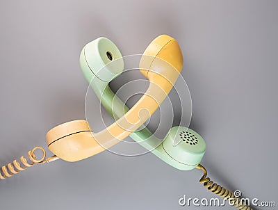 Yellow and green crossed telephone receivers with twisted cords from an old antique rotary phones on blue background Stock Photo