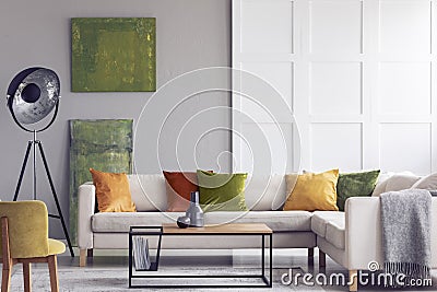 Yellow and green pillows on white settee in living room interior with paintings and lamp. Real photo Stock Photo