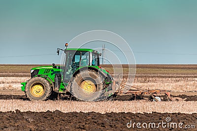 The yellow green tractor makes a deep plowing of the field Editorial Stock Photo