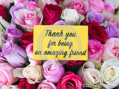 Yellow greeting card with words Thank You for Being an Amazing Friend laying on a big bouquet of colorful roses Stock Photo