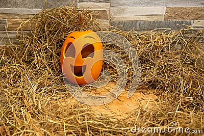 Yellow and happy smiling pumpkin. Halloween symbol on a gray stone wall background, stands on a hay and a wooden stand. Jack o Stock Photo