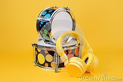 Yellow headphones and mini drum kit on the yellow background. Toy drums. Stock Photo