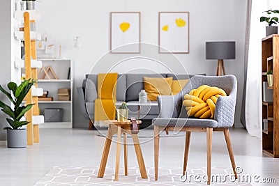 Yellow knot cushion on a gray armchair standing next to a wooden Stock Photo