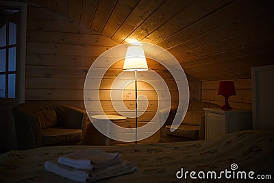 A yellow lampshade shines dimly and comfortably in the attic bedroom with a low ceiling. Lamp near the bed. Stock Photo