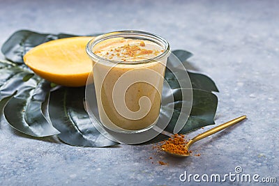 Yellow mango yogurt or smoothie on grey background. Turmeric Lassie or lassi in glass Stock Photo