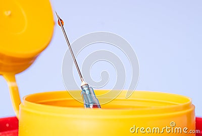 Yellow medical disposal waste box, syringe needle with red drop on the tip Stock Photo