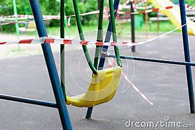 Yellow metal children's swing on a sports playground in the park wrapped with red barrier tape Stock Photo