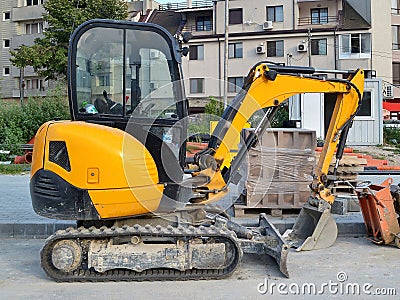 Yellow mini excavator on tracks for small construction works in hard-to-reach places or on narrow city streets Stock Photo