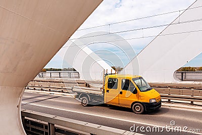 Yellow mini truck speeding over modern bridge, used in intra-city low tonnage cargo delivery Stock Photo