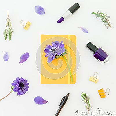 Yellow notebook, blue anemones with nail polish and lipstick on white. Flat lay Stock Photo