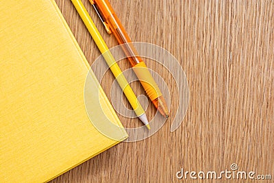 Yellow notebook, yellow pen, yellow pencil on a wooden table surface. Stationery of the same color. Office supplies. Free space Stock Photo