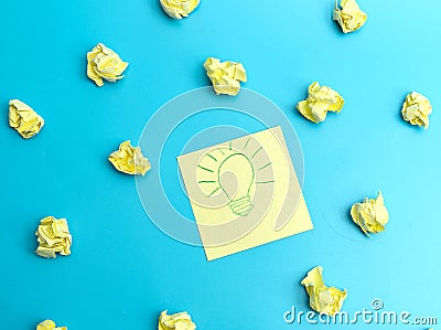 Yellow notepaper with a painted burning lamp lies on a blue background between crumpled pieces of paper. . The concept of the Stock Photo