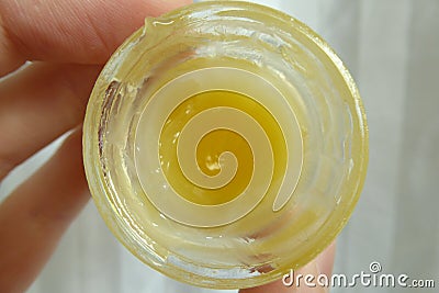 Yellow ointment in a transparent round jar . Held by the left hand . Ugly Butter disgusting substance . Beauty product treatment Stock Photo