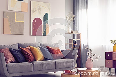 Yellow, orange, black and brown pillows on comfortable grey scandinavian sofa in bright living room interior with abstract Stock Photo