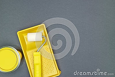 Yellow paint roller in paint tray with can of yellow paint for house renovation works on grey background Stock Photo