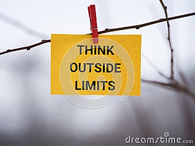 A yellow paper note with the phrase Think Outside Limits on it attached to a tree with a clothes pin Stock Photo