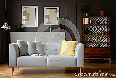 Yellow pillow on grey couch in vintage living room interior with lamp and posters. Real photo Stock Photo