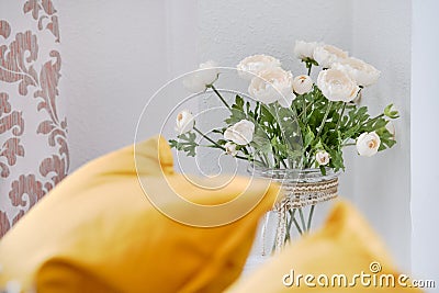 Yellow pillows on couch in living room, focus on beautiful flowers in vase white ranunculus near wall cute decoration at home Stock Photo